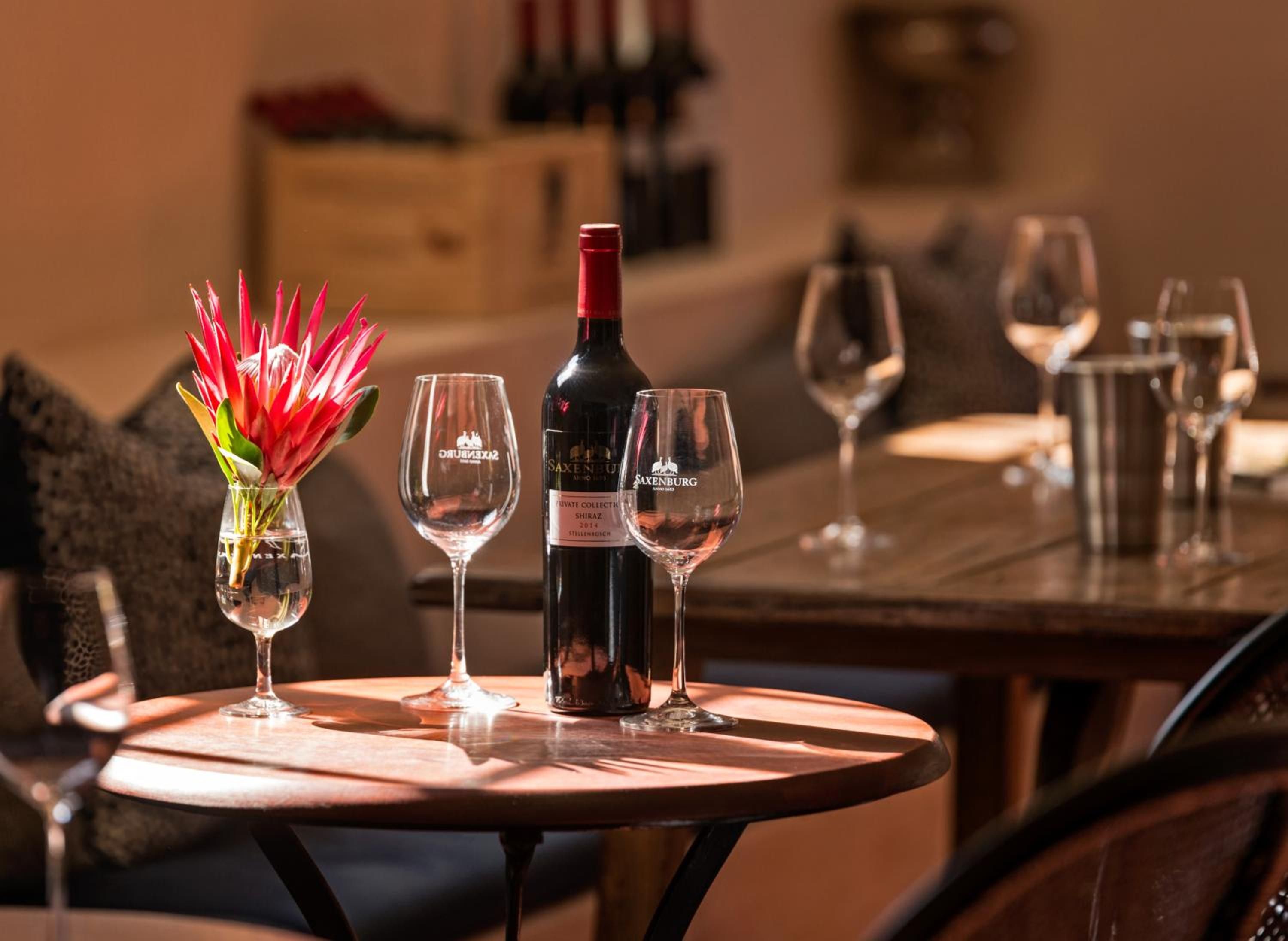 A table with a bottle of wine, two glasses, and a vase with flowers.