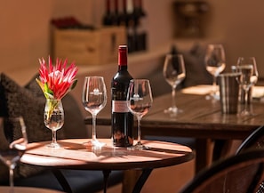A table with a bottle of wine, two glasses, and a vase with flowers. - Saxenburg Wine Farm (Cape Town)