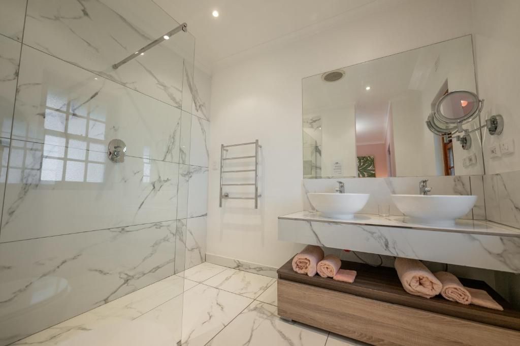 Un baño moderno con paredes de mármol, cabina de ducha de vidrio, lavamanos dobles y tocador de madera con toallas.