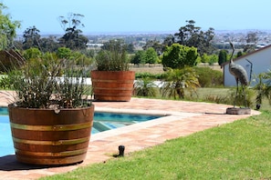 A pool area with wooden planters and a view of a cityscape in the background. - Saxenburg Wine Farm (Cape Town)