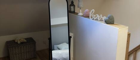 Un dormitorio tipo loft con tragaluces, un espejo de cuerpo entero, un aparador con adornos, una cama y un pequeño cómodas.