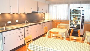 A modern kitchen with white cabinets, a sink, and a dining area with checkered tablecloths. - Hotel Vi Vintage (Stuttgart)