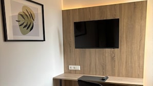 A modern office space with a desk, chair, mounted TV, and a framed artwork on the wall. - Hotel Vi Vintage (Stuttgart)