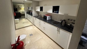 A modern kitchen with white cabinets, a black countertop, and a red fire extinguisher. - Sixty Three Hotel (Riyadh)