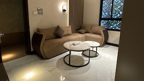 A modern living room with a beige sofa set, two marble coffee tables, and a large window with a view. - Sixty Three Hotel (Riyadh)
