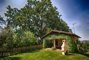 Sit on the charming porch and enjoy the serene surroundings amidst lush greenery and a wooden fence.