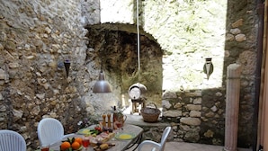 A rustic outdoor dining area with stone walls, a long table set with plates, glasses, and a variety of food items. - Villa Garibaldi. Beautiful mountain town in wine area ½ hour from Rome and beach (Cori)