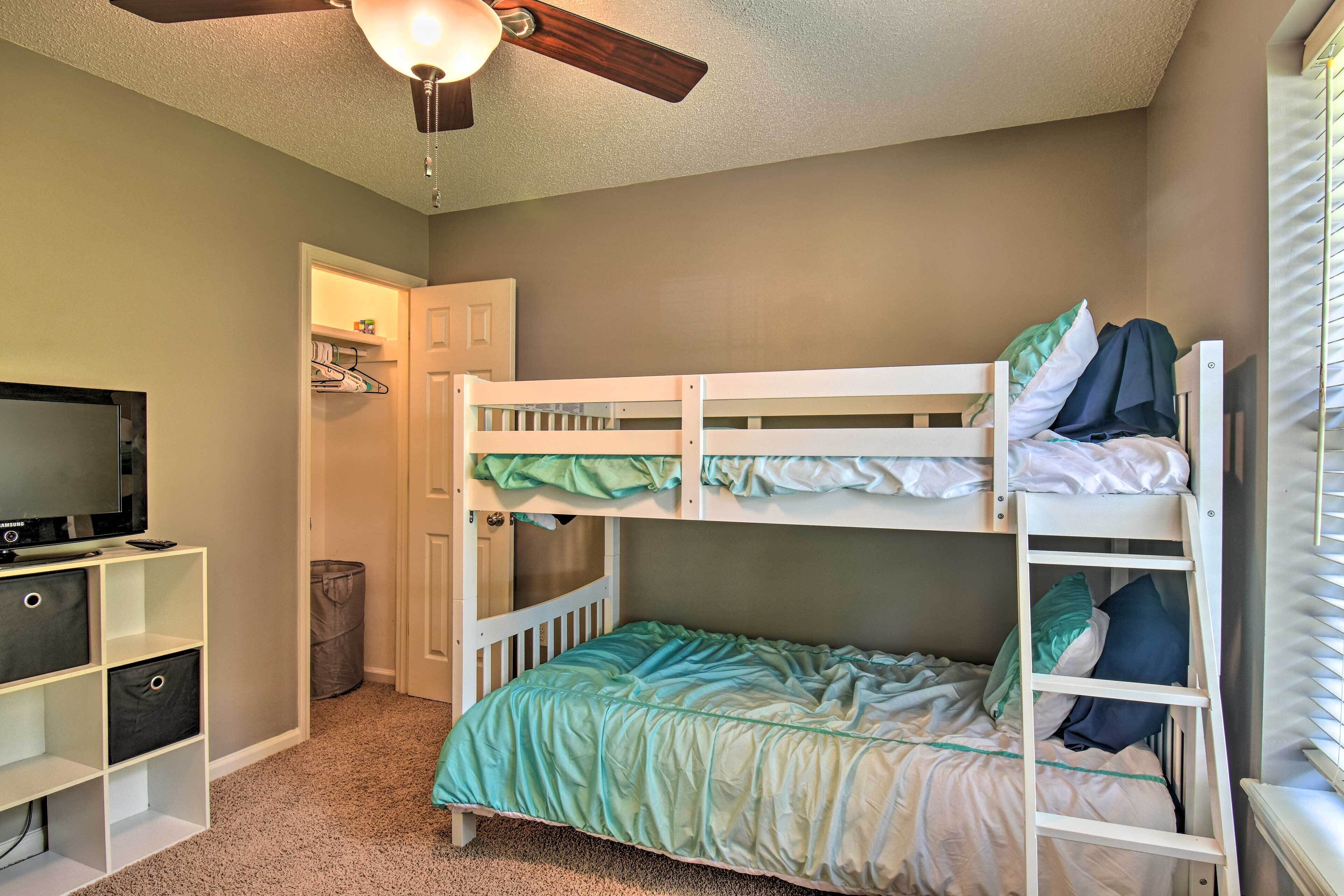 A bunk bed with a ladder, a TV on a stand, a closet, and a ceiling fan.