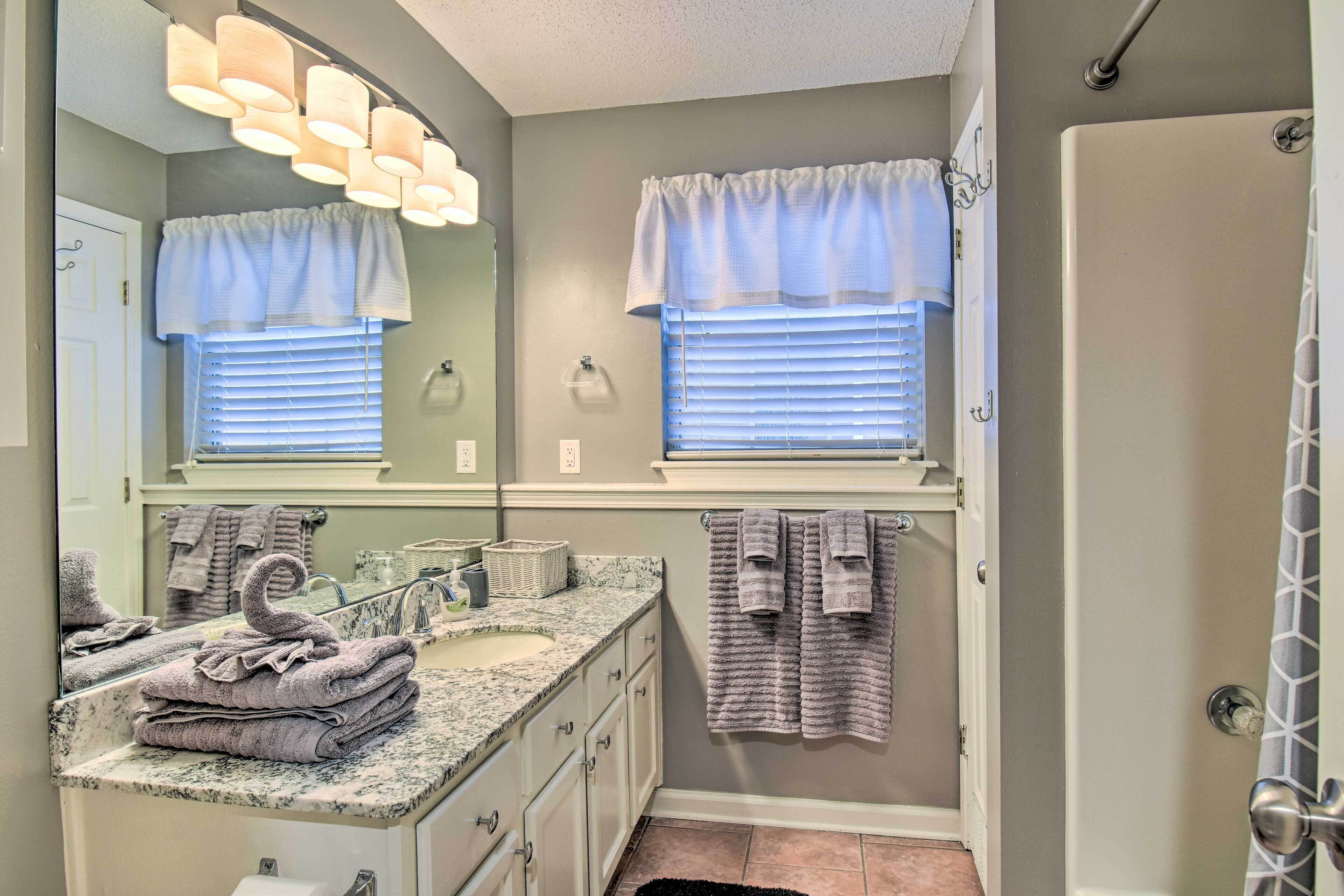 A bathroom with a sink, mirror, towel rack, and a shower area.