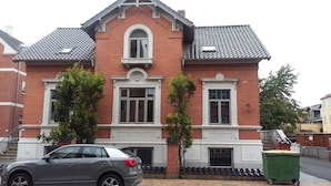 A two-story brick house with a tiled roof, a central entrance with a small porch, and a car parked in front. - Thorsgade 1A (Odense)