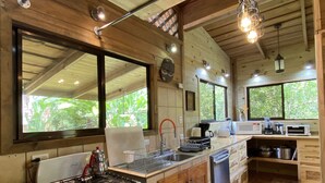Une cuisine équipée d’une cuisinière, d’un évier et de meubles en bois. Des fenêtres offrent une vue sur la verdure environnante.