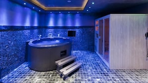 A modern bathroom with a large bathtub, a wooden bench, and a tiled floor. - Miramonte Chalet Hotel Spa (Edessa)
