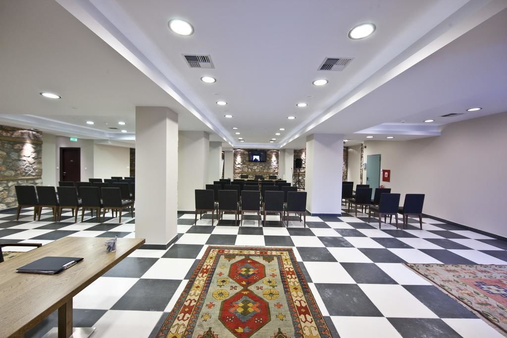 Une salle de conférence avec un sol à carreaux, des chaises noires et blanches, une table en bois et une moquette à motifs.
