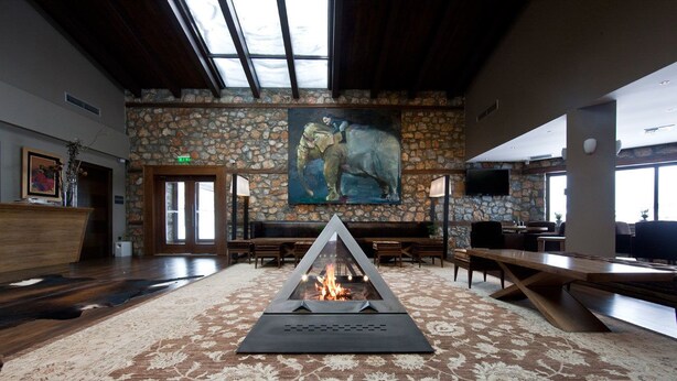 A spacious lobby with a stone wall, a painting, a fire feature, and a large wooden table. - Miramonte Chalet Hotel Spa (Edessa)