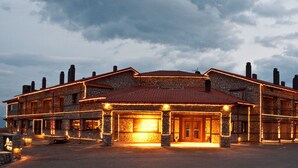 A large, multi-story stone building with a red-tiled roof, multiple chimneys, and a well-lit entrance. - Miramonte Chalet Hotel Spa (Edessa)