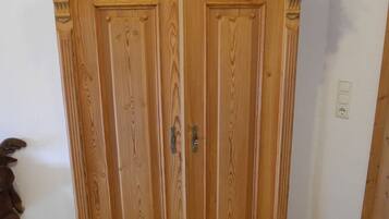 A wooden armoire with two doors and a small shelf at the top, featuring a decorative floral arrangement.