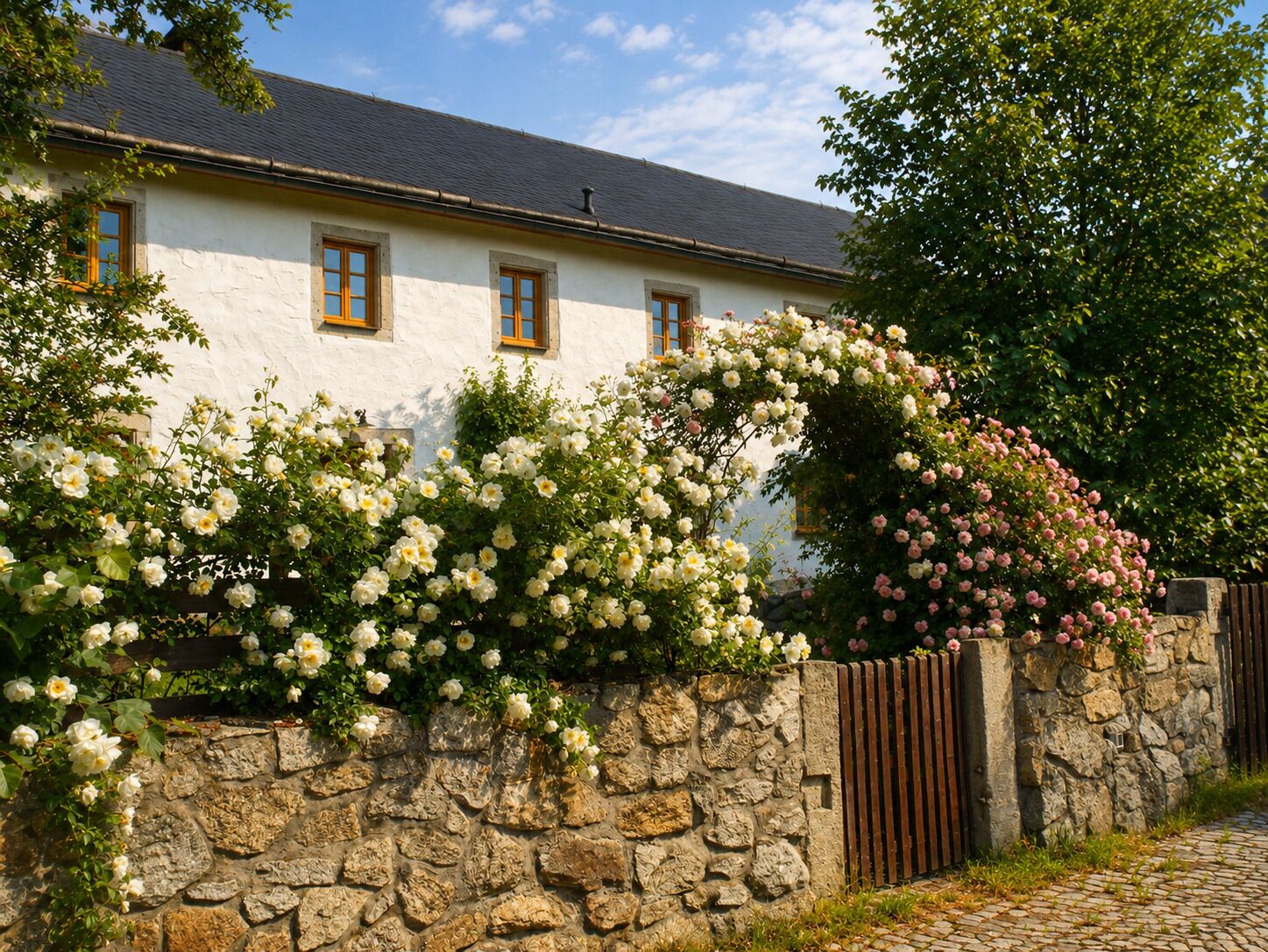 A white building with a stone wall and a wooden gate.