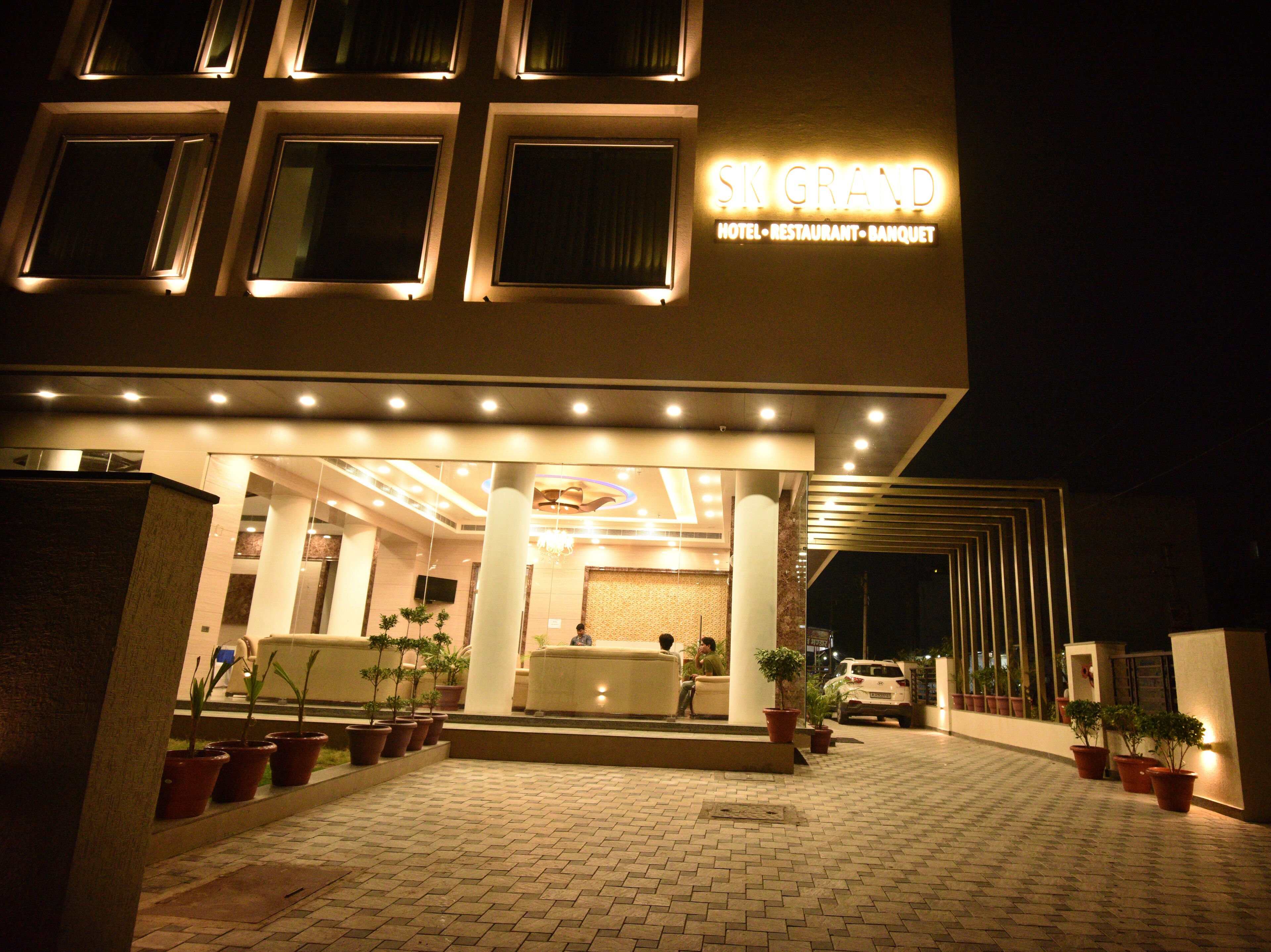 A hotel entrance with a reception desk, potted plants, and a car parked outside.