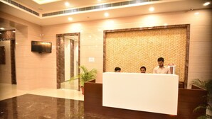 Balcão de recepção em saguão de hotel com piso de mármore, televisão de tela plana na parede e revestimento padronizado atrás do balcão.