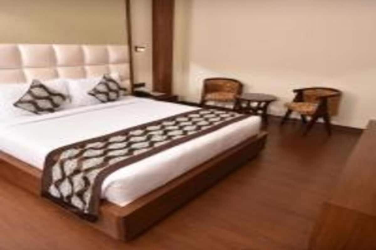 Quarto de hotel com uma cama grande, duas cadeiras, uma mesinha e piso de madeira.