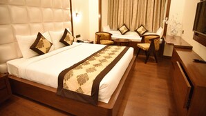 Quarto de hotel com uma cama grande, duas cadeiras, uma mesinha, televisão e janela com cortinas.