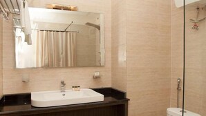 A bathroom with a white sink, a mirror, a shower, and a towel rack.
