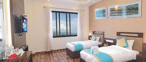 A hotel room with two beds, a TV, a window with curtains, and artwork on the wall.