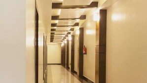 A long, well-lit hallway with a reflective floor, leading to a door with a fire extinguisher on the wall.