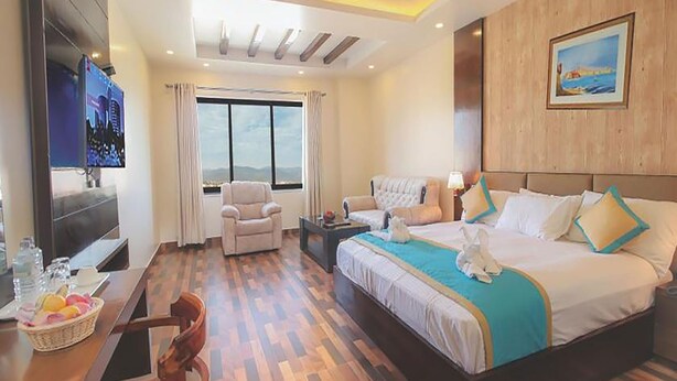 A hotel room with a large bed, a desk with a TV, a chair, and a window with curtains.