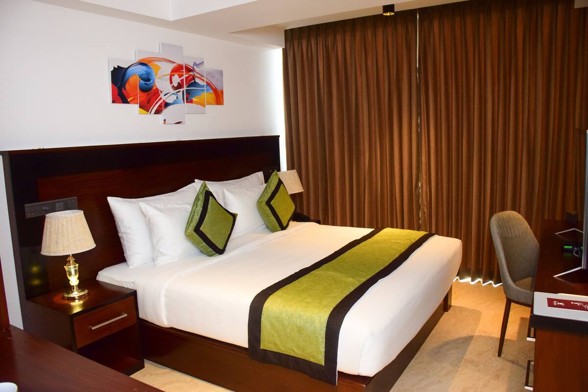 A hotel room with a large bed, a desk, a chair, a lamp, and a painting on the wall.