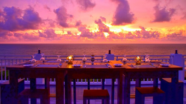 Mesa lista para cenar con vista al océano y al atardecer.