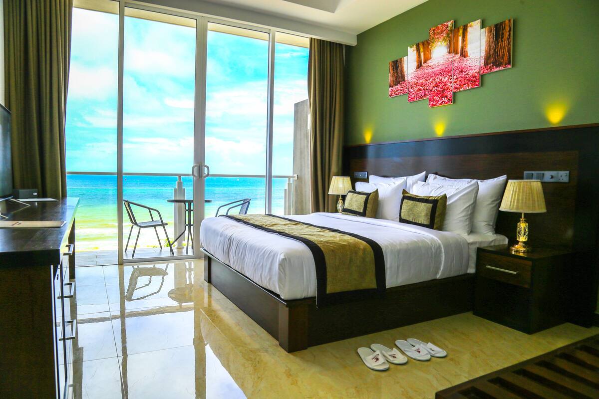 A hotel room with a large bed, a desk, a chair, and a view of the ocean.