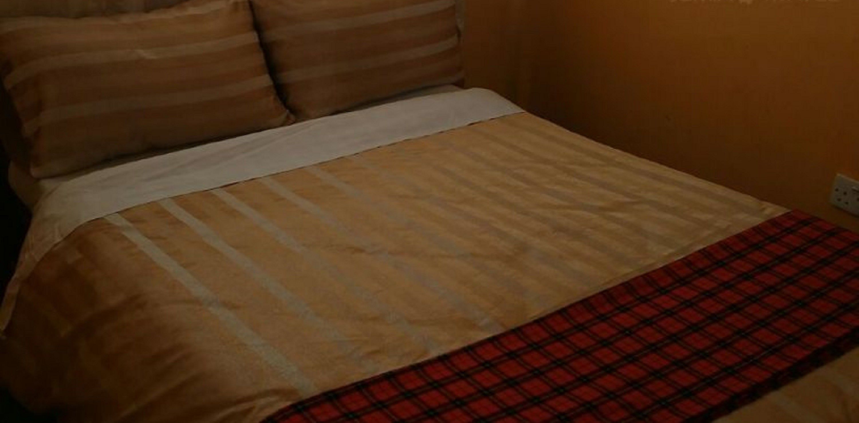 A bed with a striped bedspread and a plaid blanket.