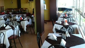 Comedor con mesas y sillas, una barra de buffet y vistas a través de amplios ventanales.