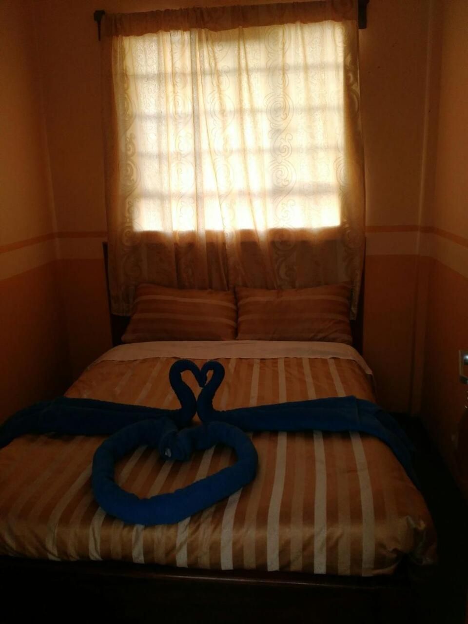 A hotel room with a bed, striped bedding, and a heart-shaped towel arrangement.