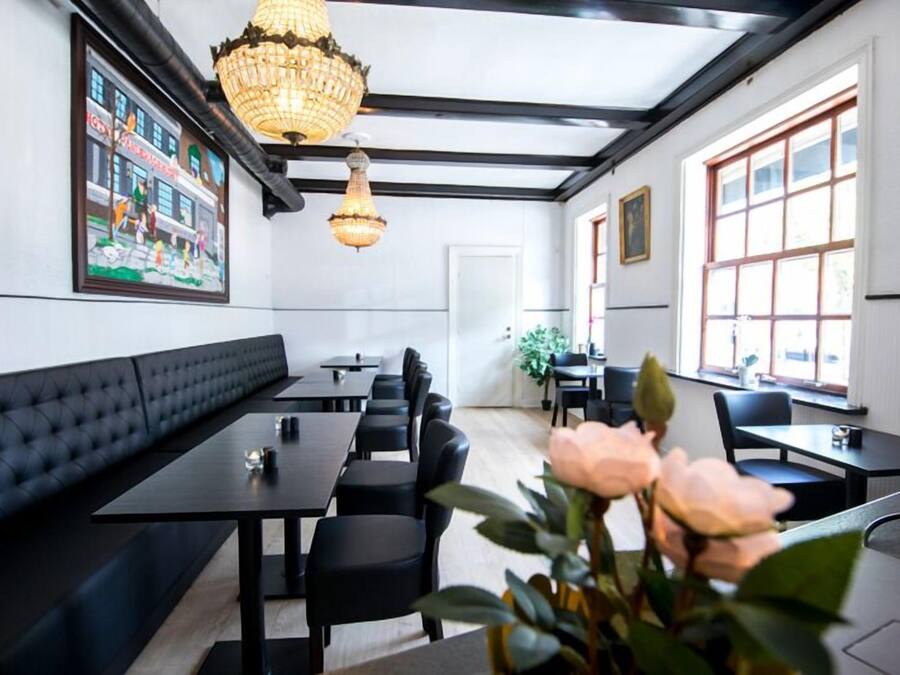 A restaurant with black leather booths, rectangular tables, and black chairs. There are two chandeliers hanging from the ceiling.