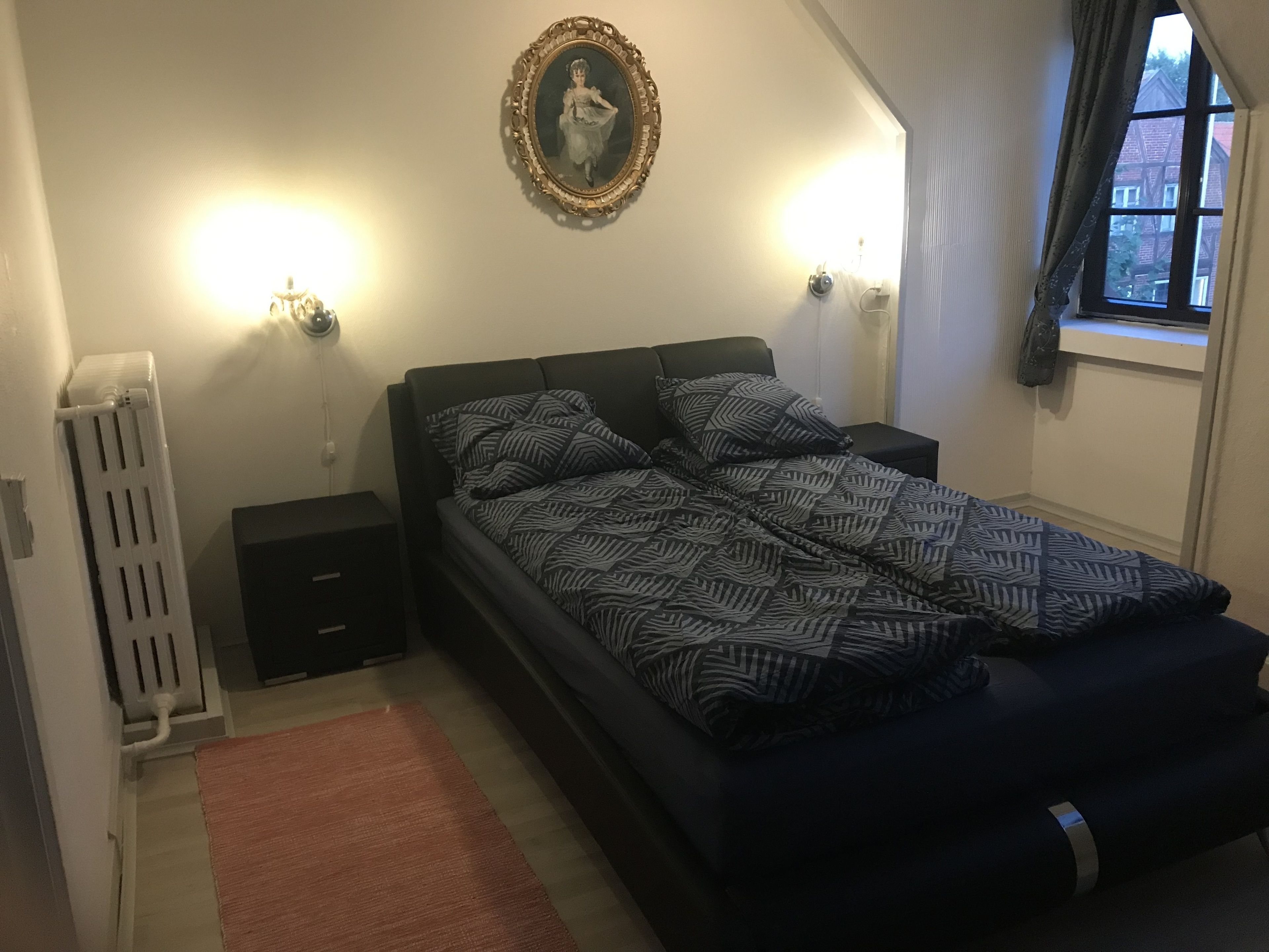 Una camera da letto con un letto, un comodino, un termosifone e una finestra con tende.