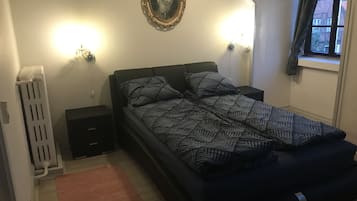 Una camera da letto con un letto, un comodino, un termosifone e una finestra con tende.