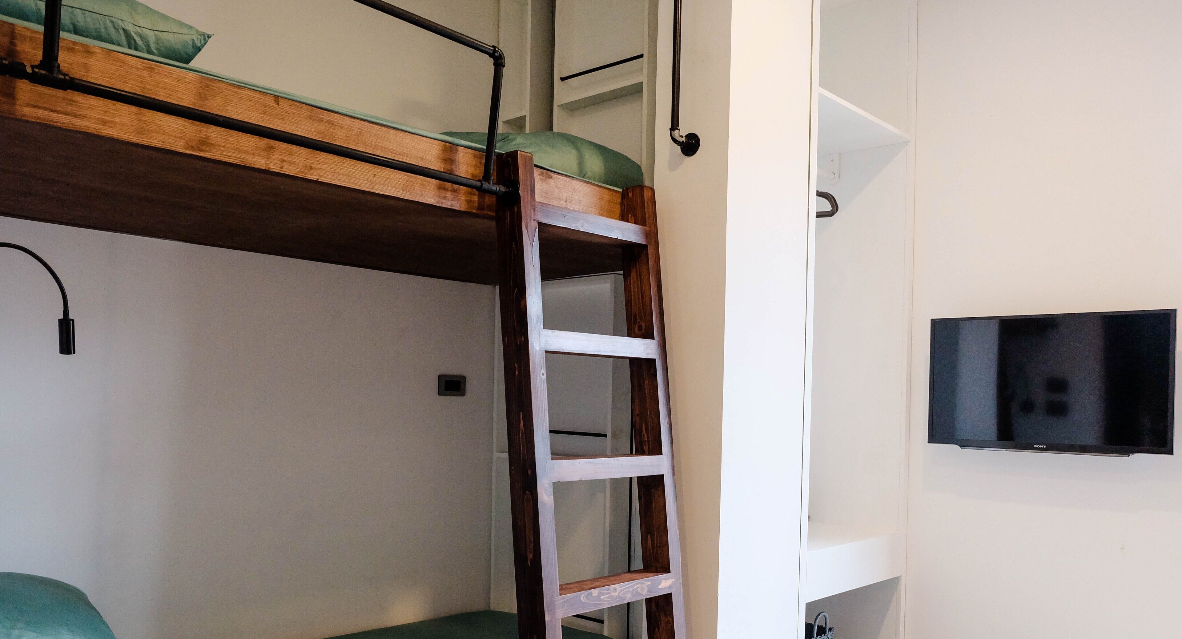 Una cama litera con escalera, un televisor en la pared y un estante pequeño.