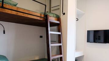 Una cama litera con escalera, un televisor en la pared y un estante pequeño.