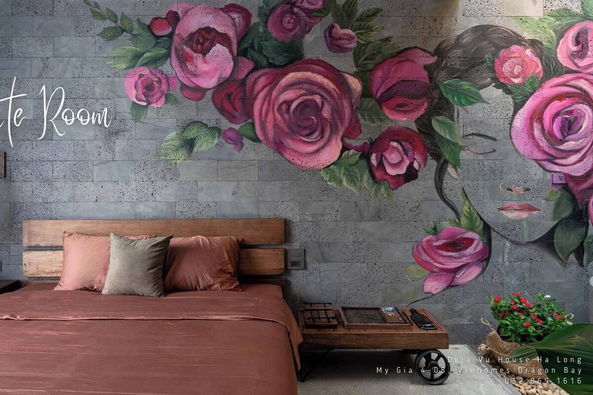 A bedroom with a bed, pillows, a nightstand, a wall-mounted lamp, and a decorative wall mural.