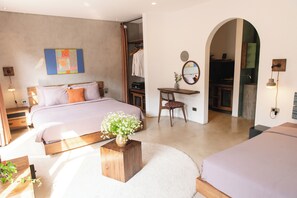 Un dormitorio con cama, mesita de noche y un escritorio pequeño con silla. Hay un espejo en la pared y una puerta que da a otra habitación.