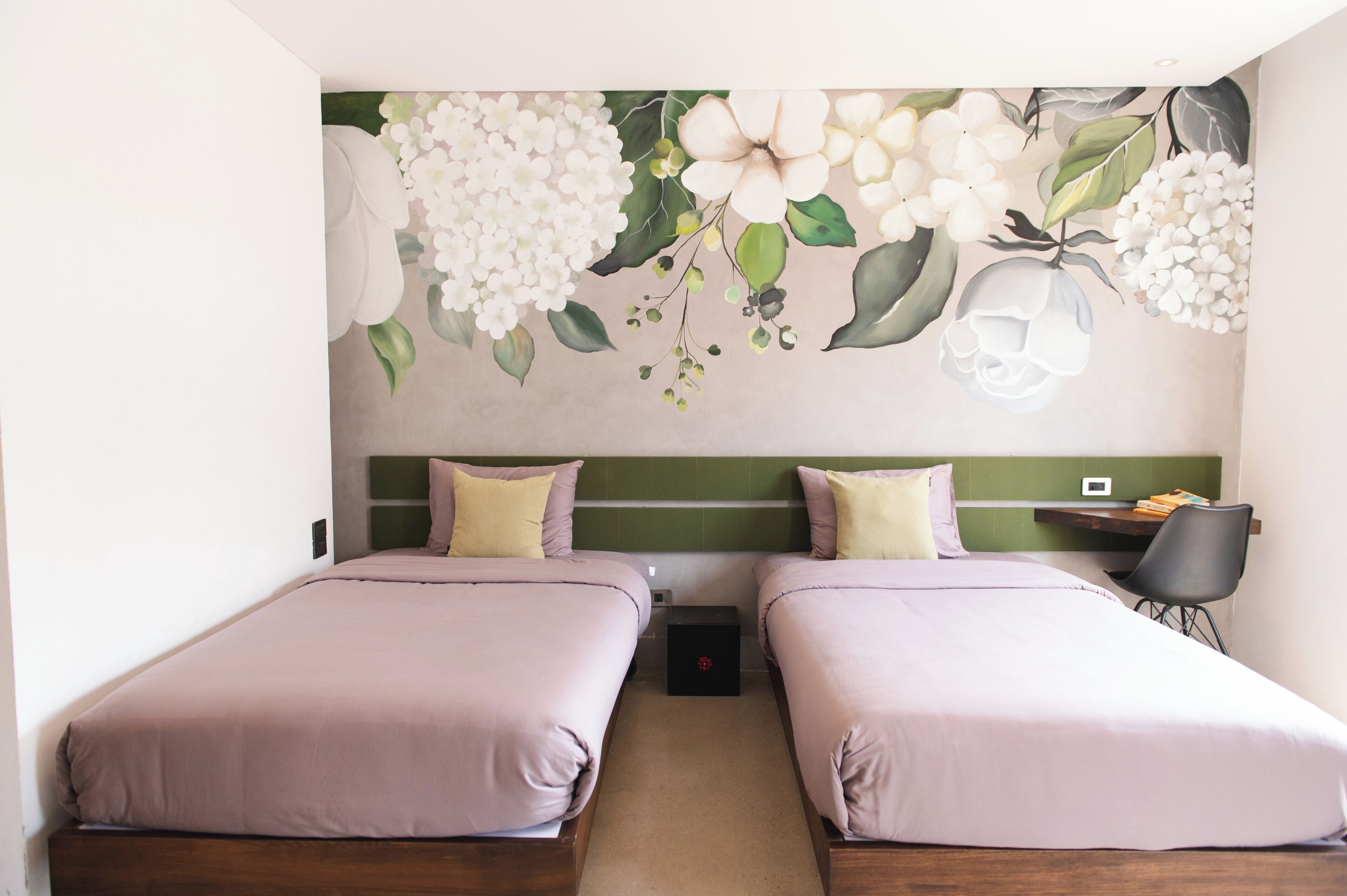 A hotel room with two beds, a desk, and a wall mural of flowers.