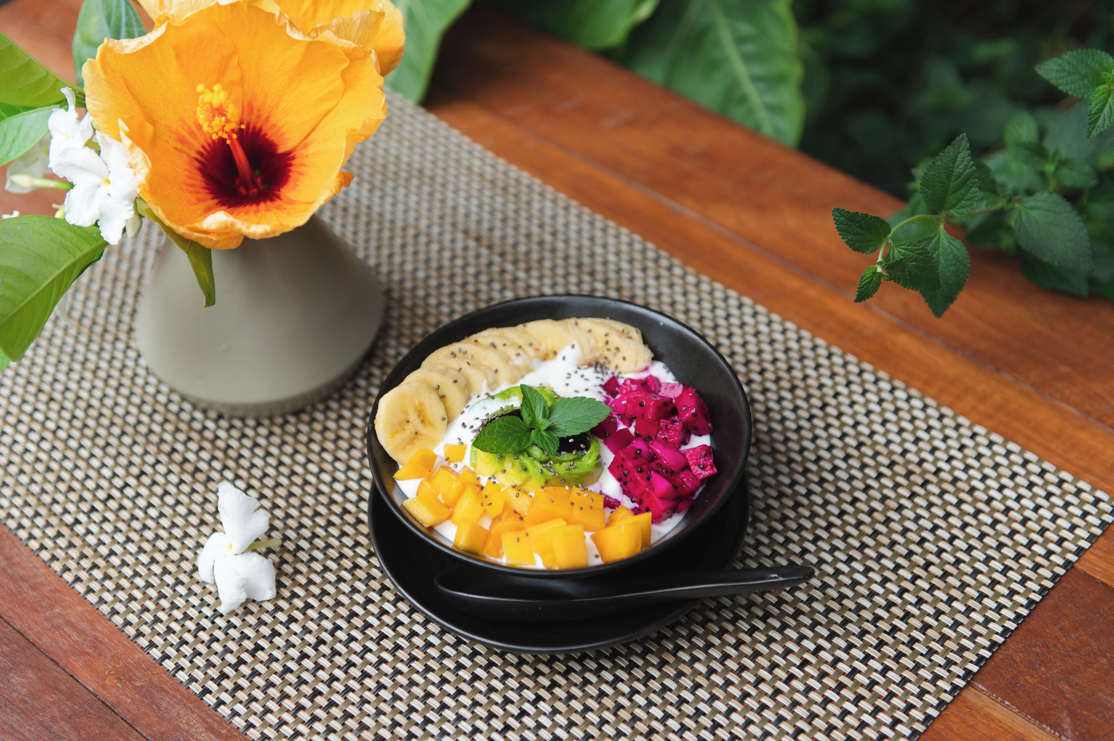 Una ciotola di insalata di frutta con mango, pitaya e banana su un tappetino di vimini.