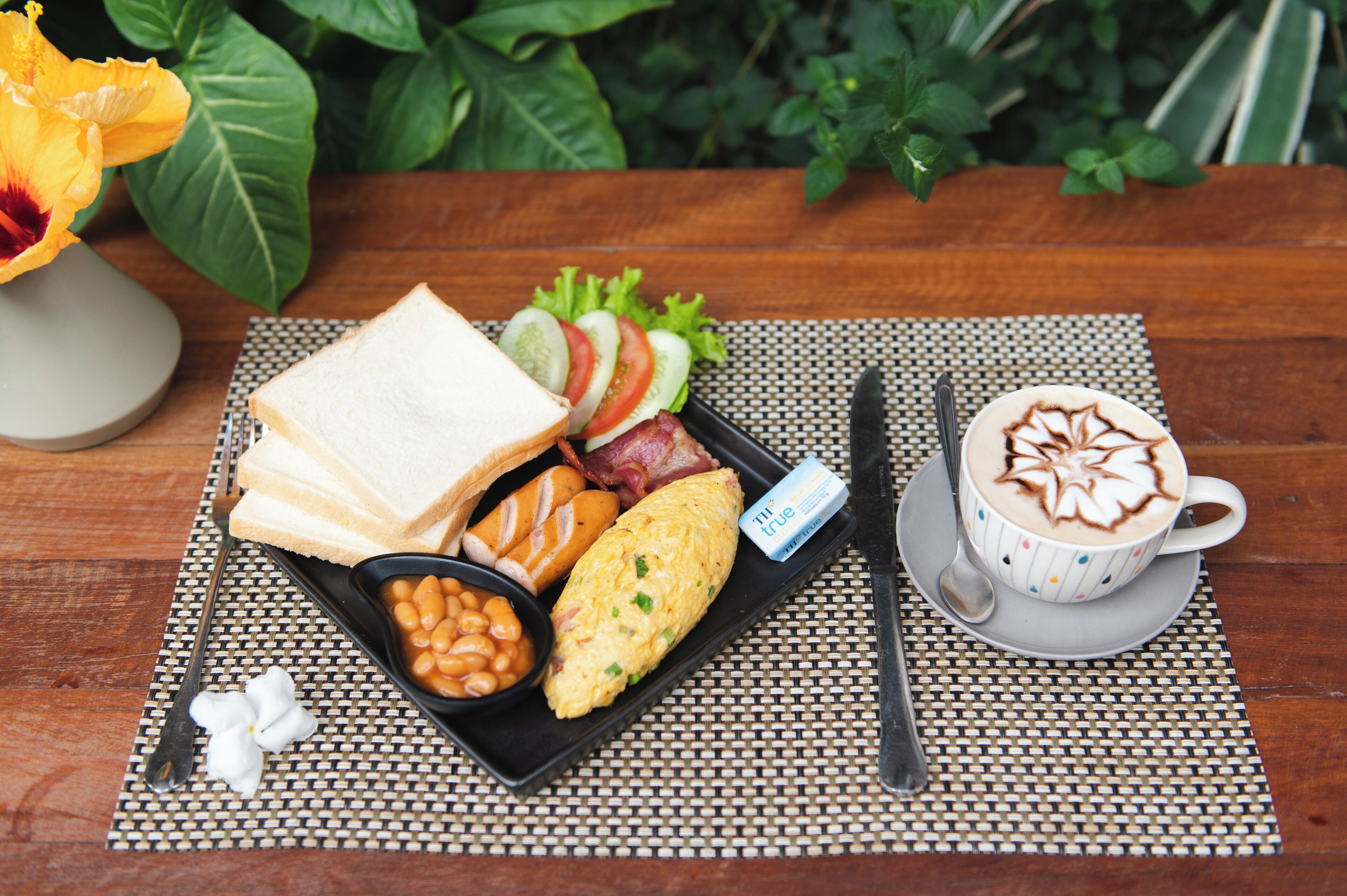 A breakfast tray with toast, eggs, beans, bacon, and a cup of coffee with latte art.
