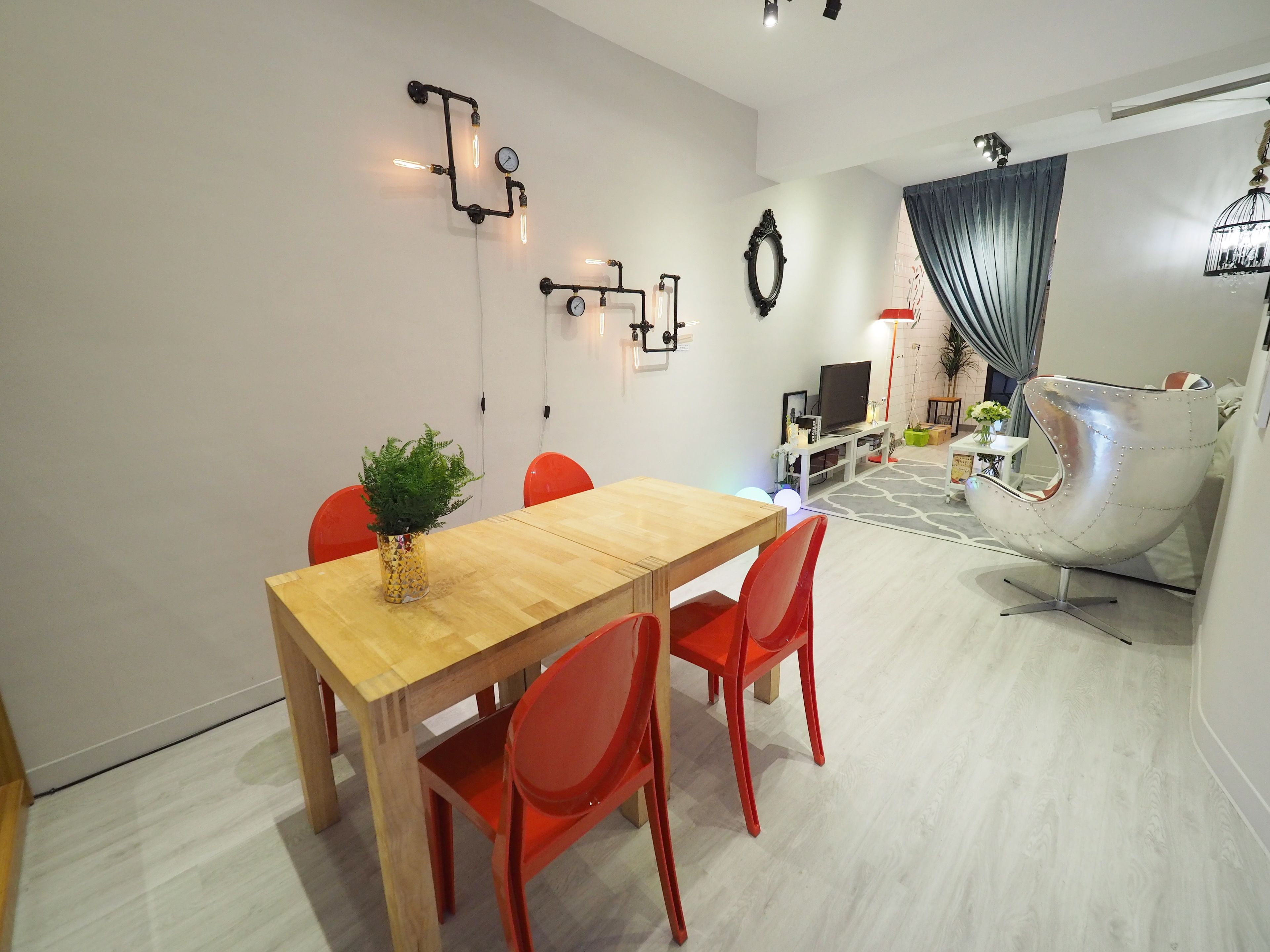 A modern living room with a wooden dining table, red chairs, a unique metallic chair, a television, and a decorative mirror.