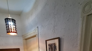 Ein schmaler Flur mit einer weißen Tür, einem gerahmten Bild von einem Elefanten und einer Pendelleuchte.