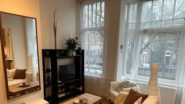 Ein Wohnzimmer mit einer Couch, einem Couchtisch, einem Fernseher und einem großen Fenster mit Blick auf die Straße.