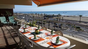 A dining area with a table set for two, overlooking a beach and a busy road. - THE PATIO APARTMENT FACING THE SEA (Canet-en-Roussillon)