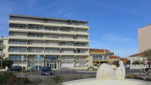 A multi-story building with balconies, a parking area, and a sculpture in the foreground. - THE PATIO APARTMENT FACING THE SEA (Canet-en-Roussillon)